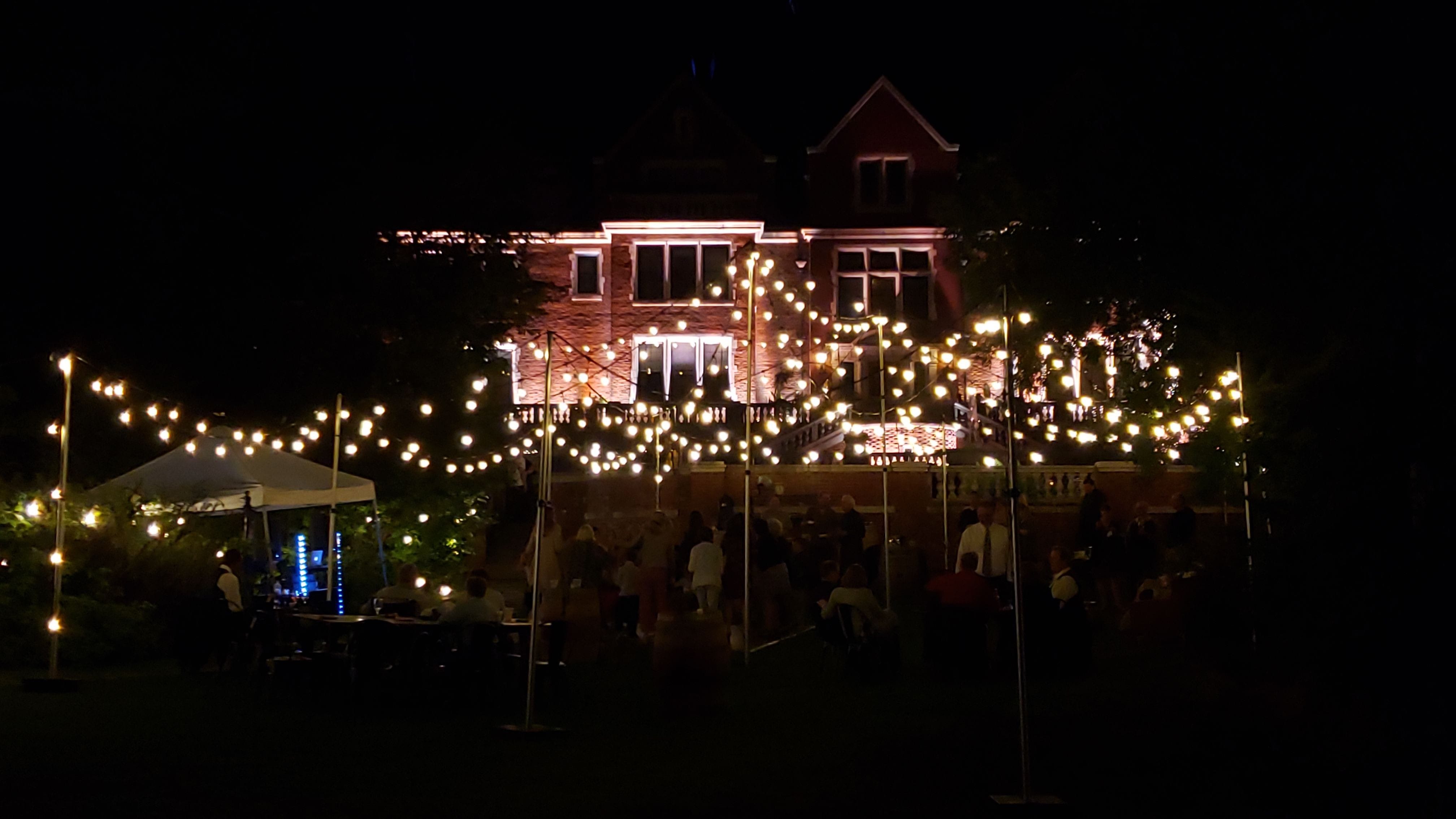 The back side of Glensheen Mansion lit for a wedding in the garden with a bistro tent.
